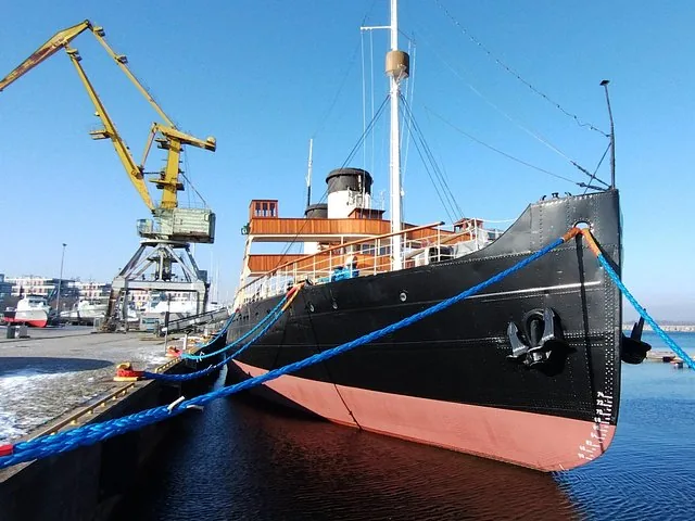 Large black ship docked at a port with a yellow crane.