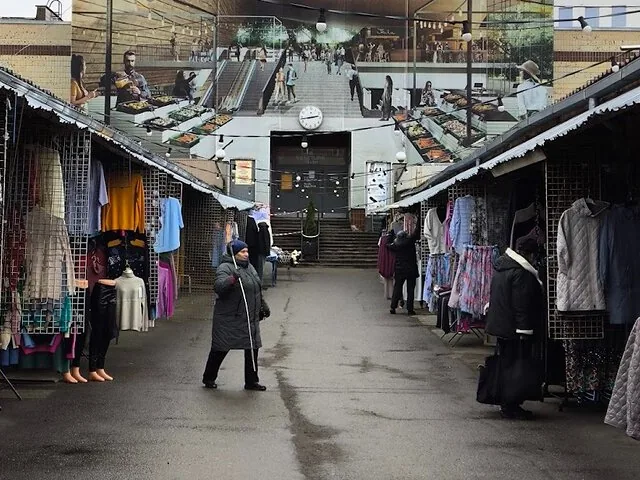 Outdoor market with stalls selling clothing, people walking.