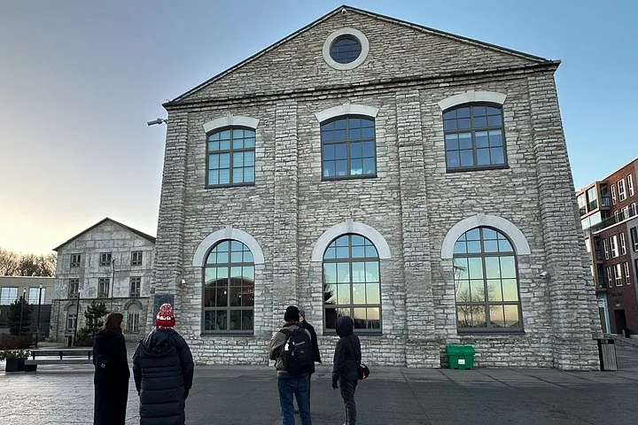 Group of people standing in front of a stone building with arched windows.